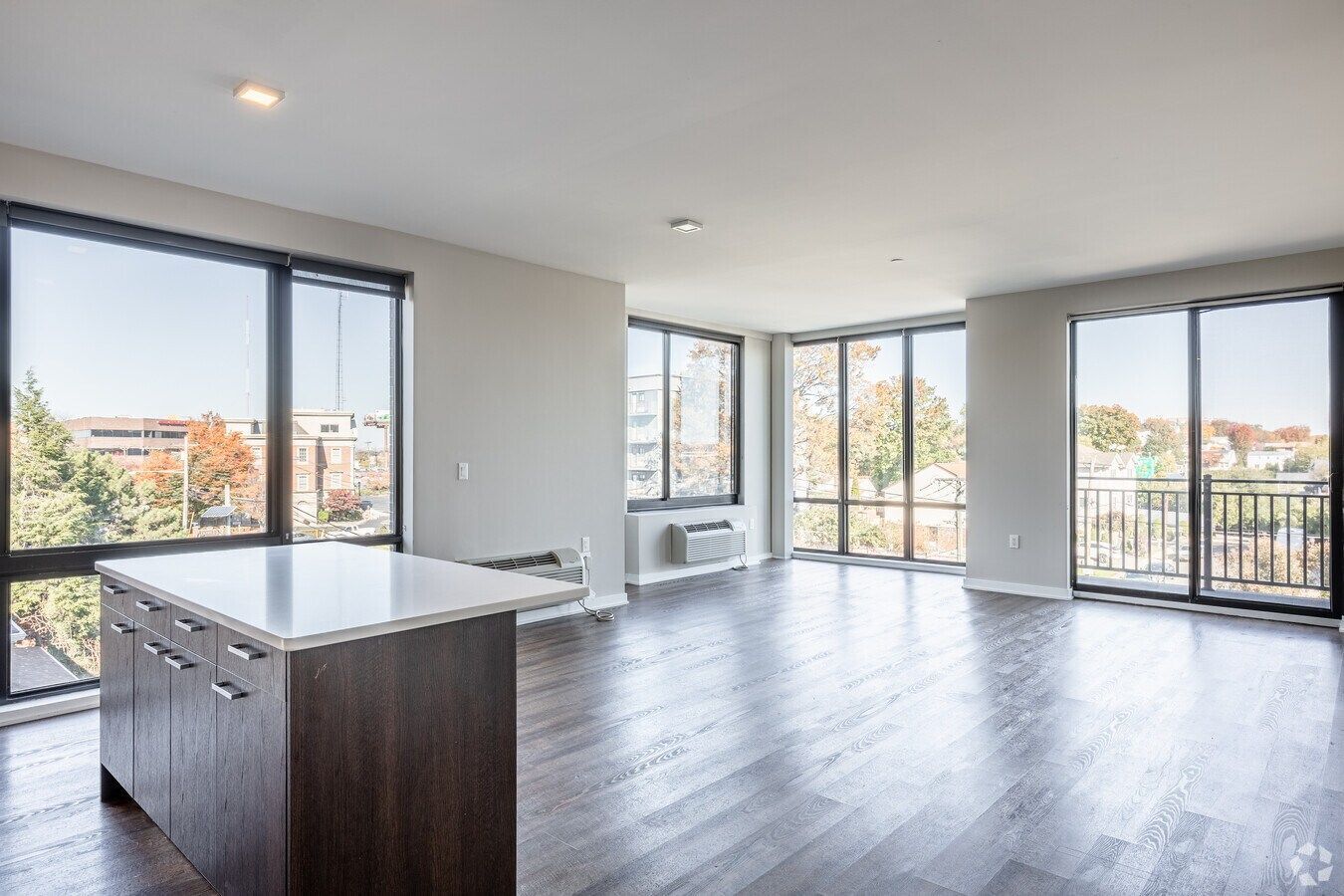 Bright empty modern apartment with large windows, balcony, and kitchen island.