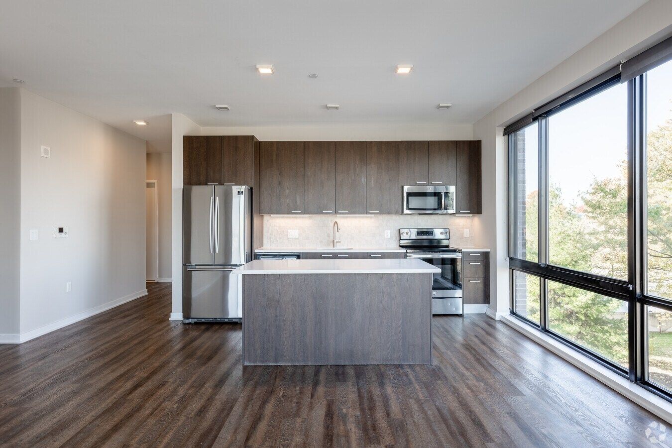 Modern kitchen with island, stainless steel appliances, wood floors, and large windows overlooking trees