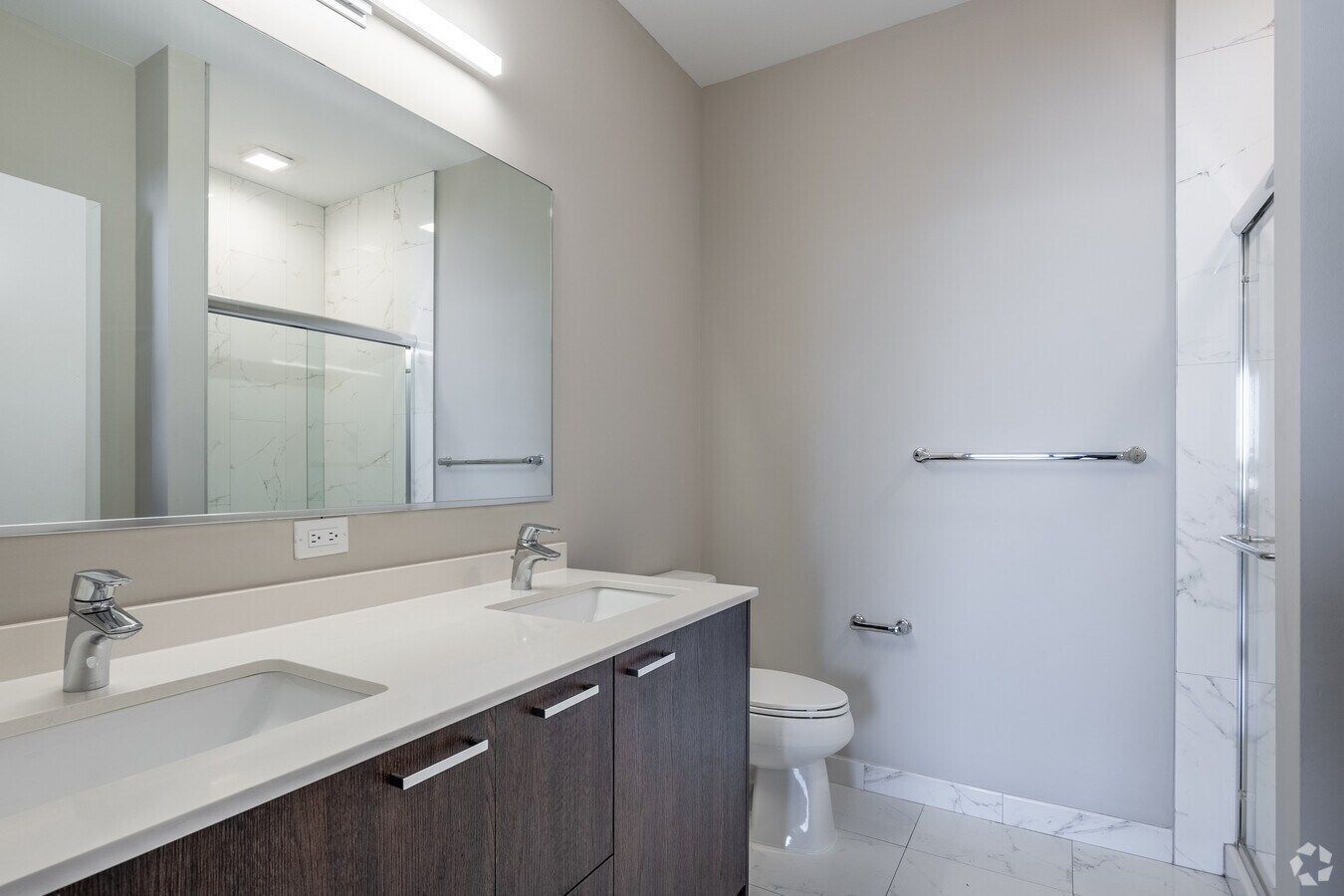 Modern bathroom with double vanity, large mirror, toilet, and glass shower door