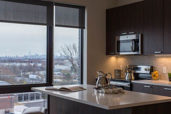 Modern kitchen with dark cabinets, island, and large window overlooking a city skyline