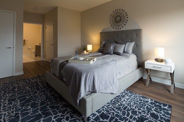 Modern bedroom with a gray bed, nightstands, and patterned rugs on a beige floor