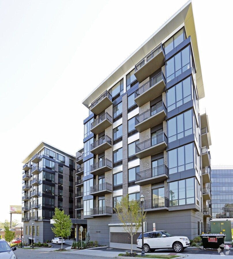 Modern apartment buildings with glass balconies on a sunny street, with parked cars and trees
