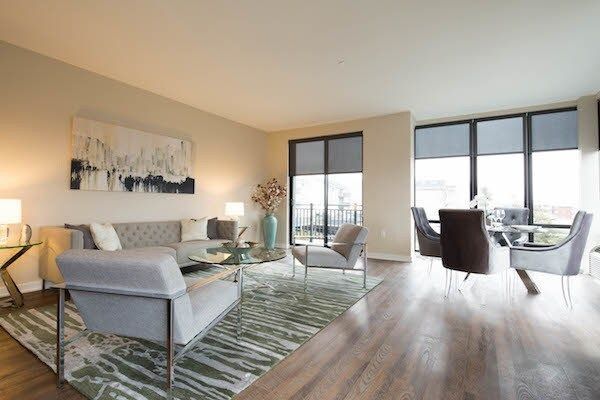 Bright modern living room with sectional sofa, rug, chairs, and large windows overlooking a city view