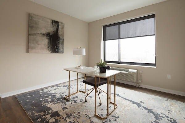 Minimal home office with desk, chair, lamp, abstract wall art, and large window on patterned rug