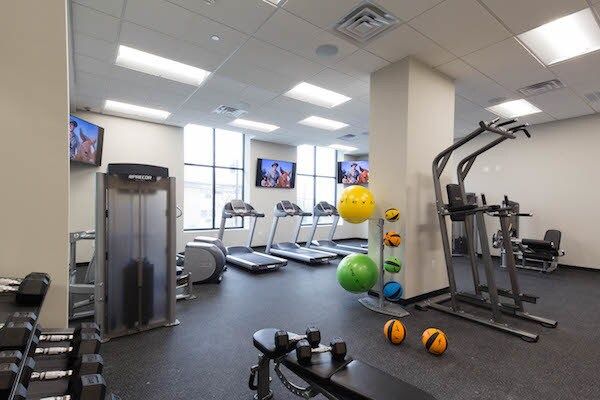 Gym interior with treadmills, weight machines, and exercise balls under bright ceiling lights