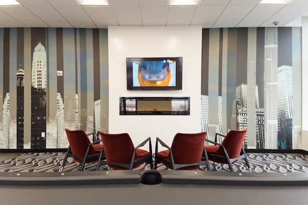 Modern lounge with red chairs, patterned carpet, striped wall panels, and two wall-mounted screens