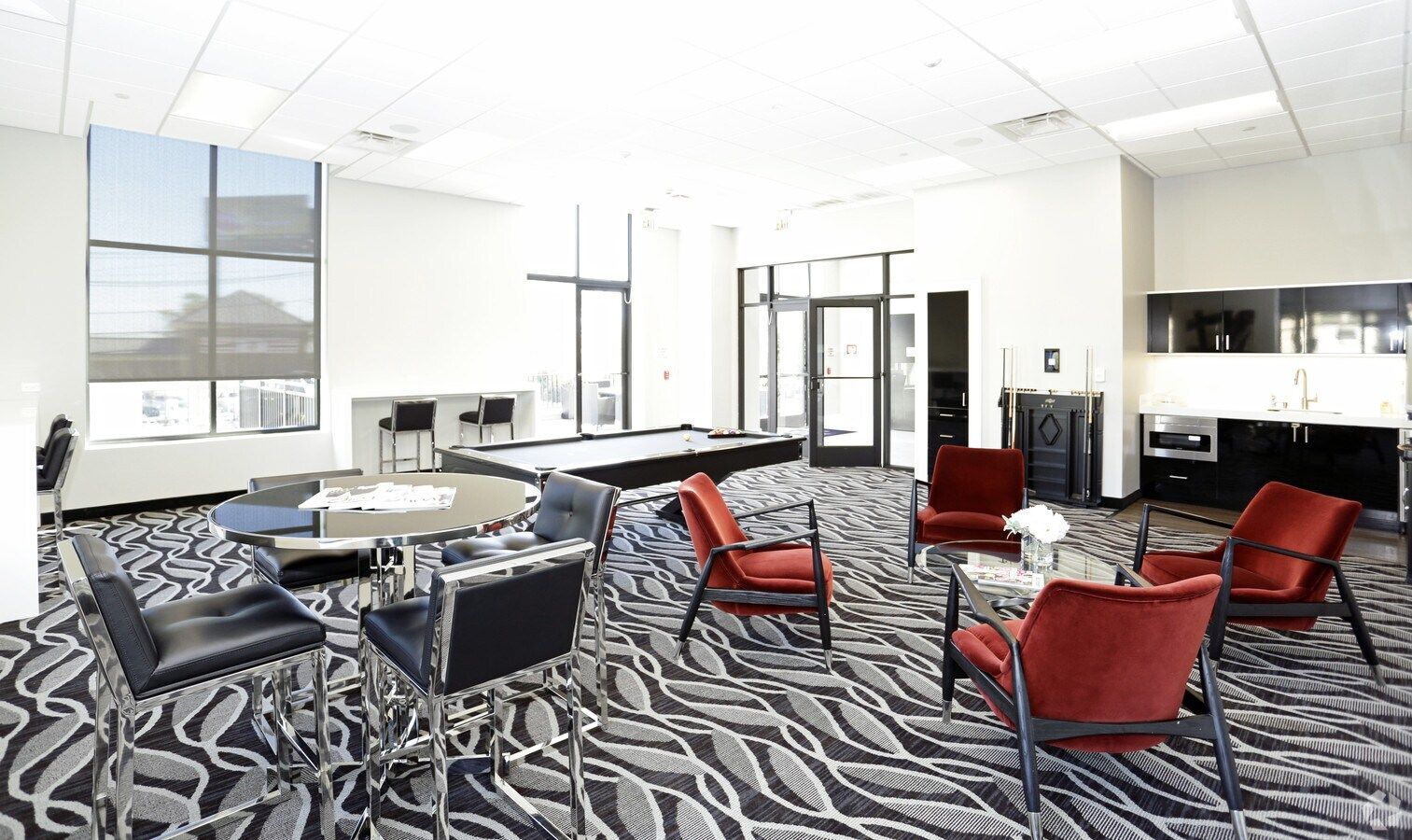 Modern lounge with red and black chairs, patterned carpet, sofas, and large windows in a bright room