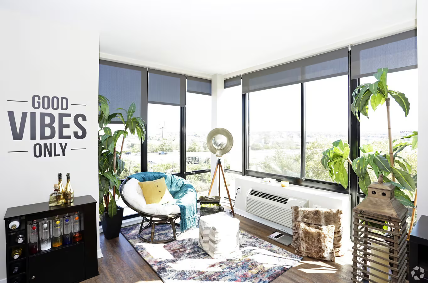 Bright sunroom with corner windows, white couch, plants, and “GOOD VIBES ONLY” wall art