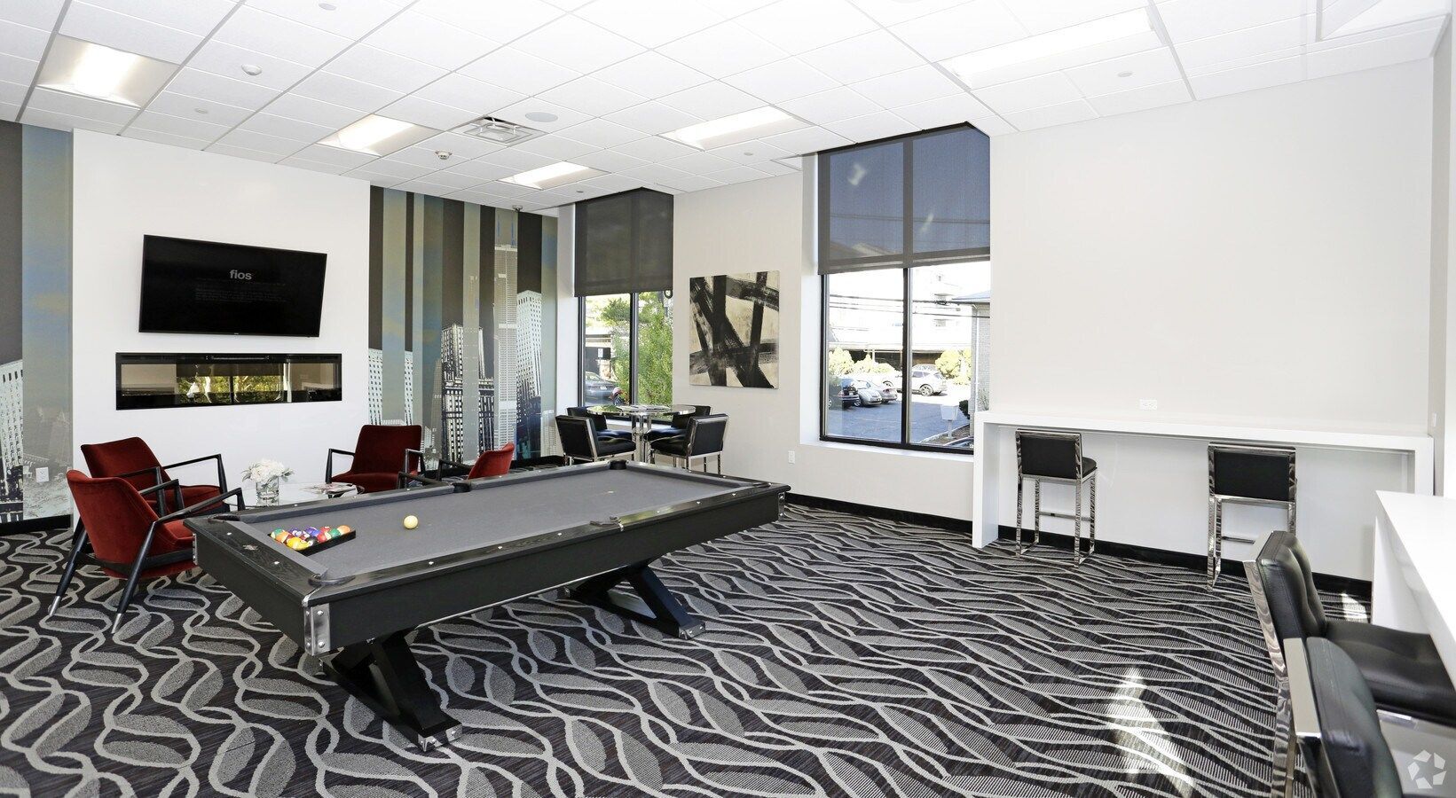 Modern meeting room with pool table, red chairs, wall TV, and large windows overlooking the city.
