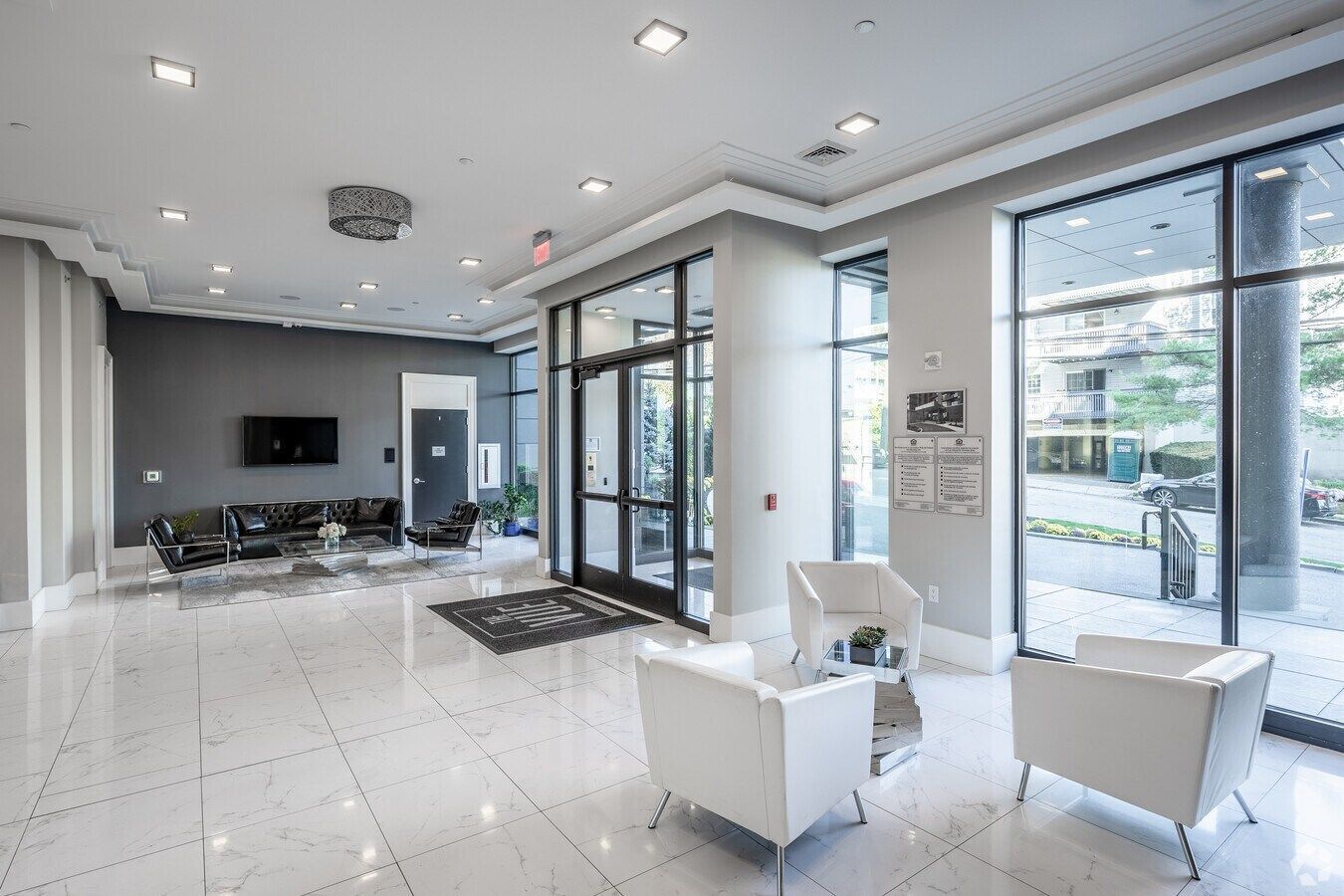 Modern white lobby with glossy tile floors, lounge chairs, and floor-to-ceiling windows looking outside