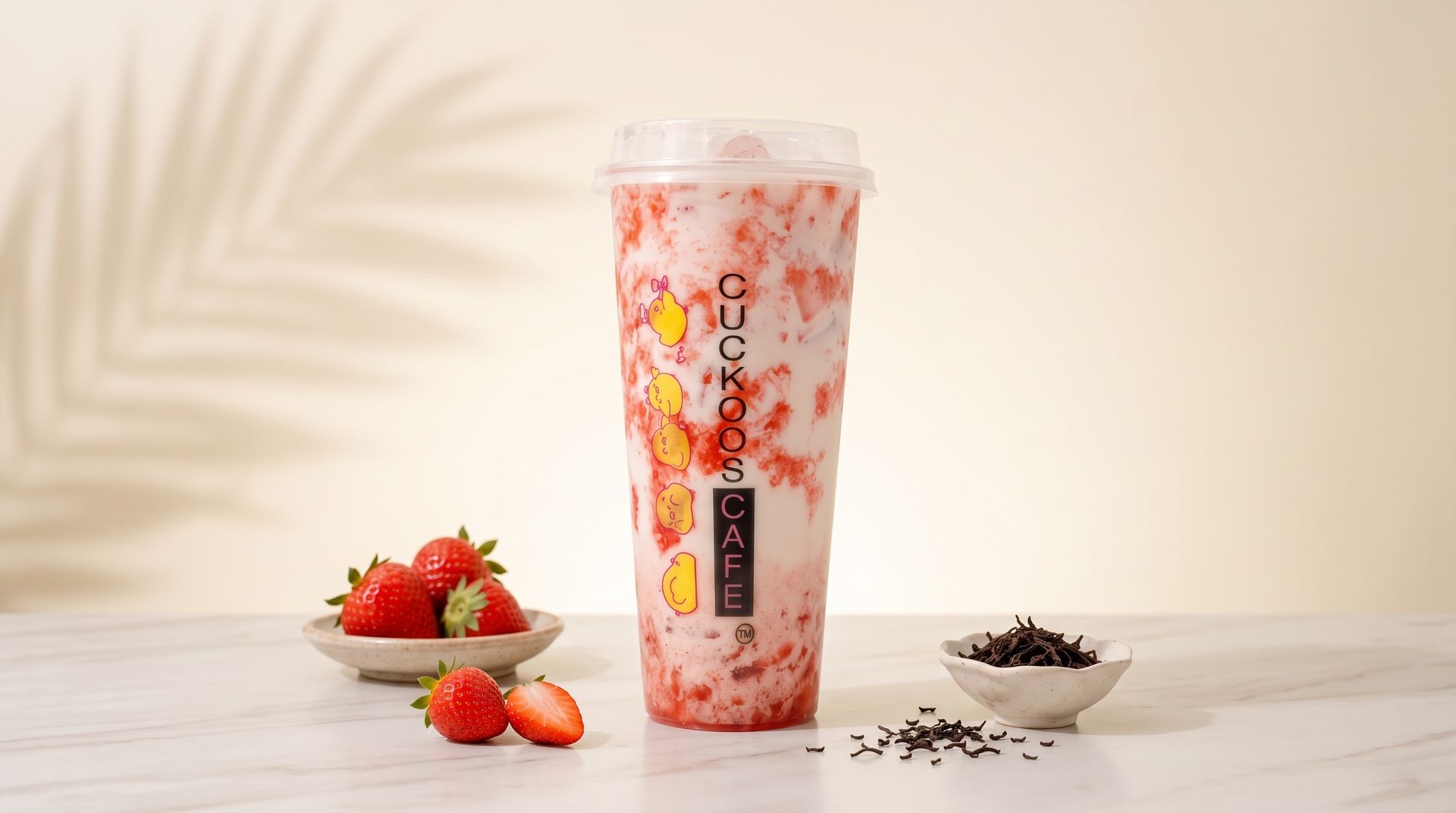 Pink strawberry milk tea in a clear cup with strawberries and tea leaves on a light background