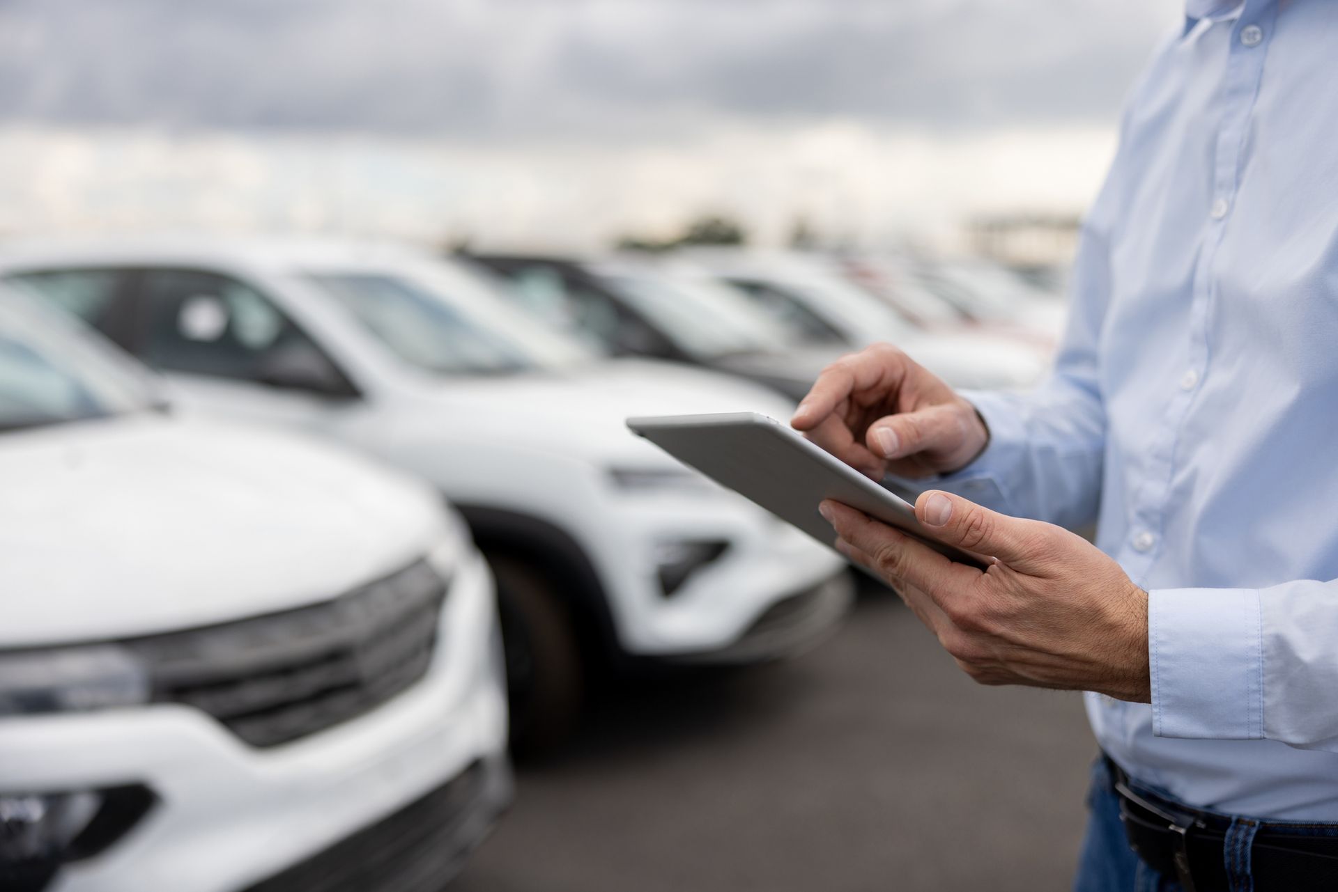 Un uomo tiene in mano un tablet davanti a una fila di auto bianche.