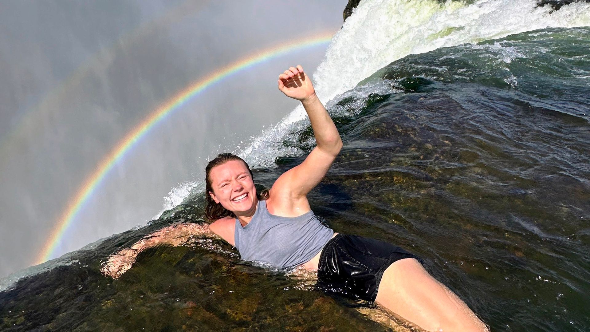 A woman is laying in the water with a rainbow in the background.