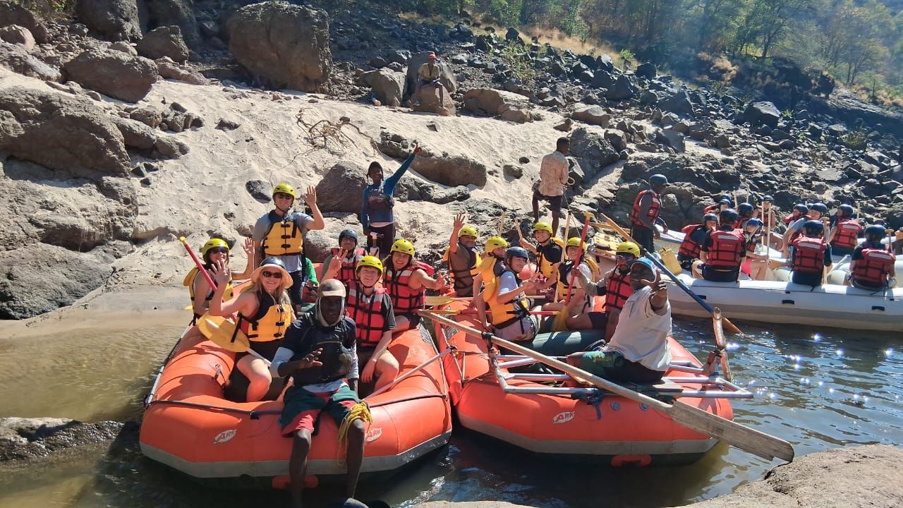 Four people in orange life vests and yellow helmets whitewater rafting in a orange raft