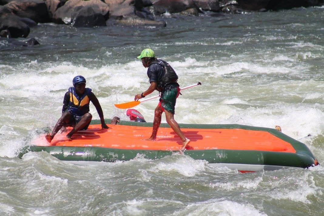 A man is paddling a raft in a river while another man sits on the raft.