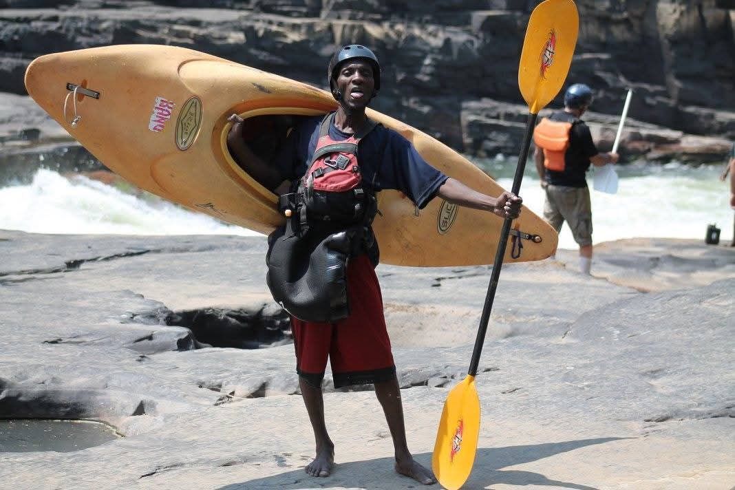 A man holding a yellow kayak and a yellow paddle