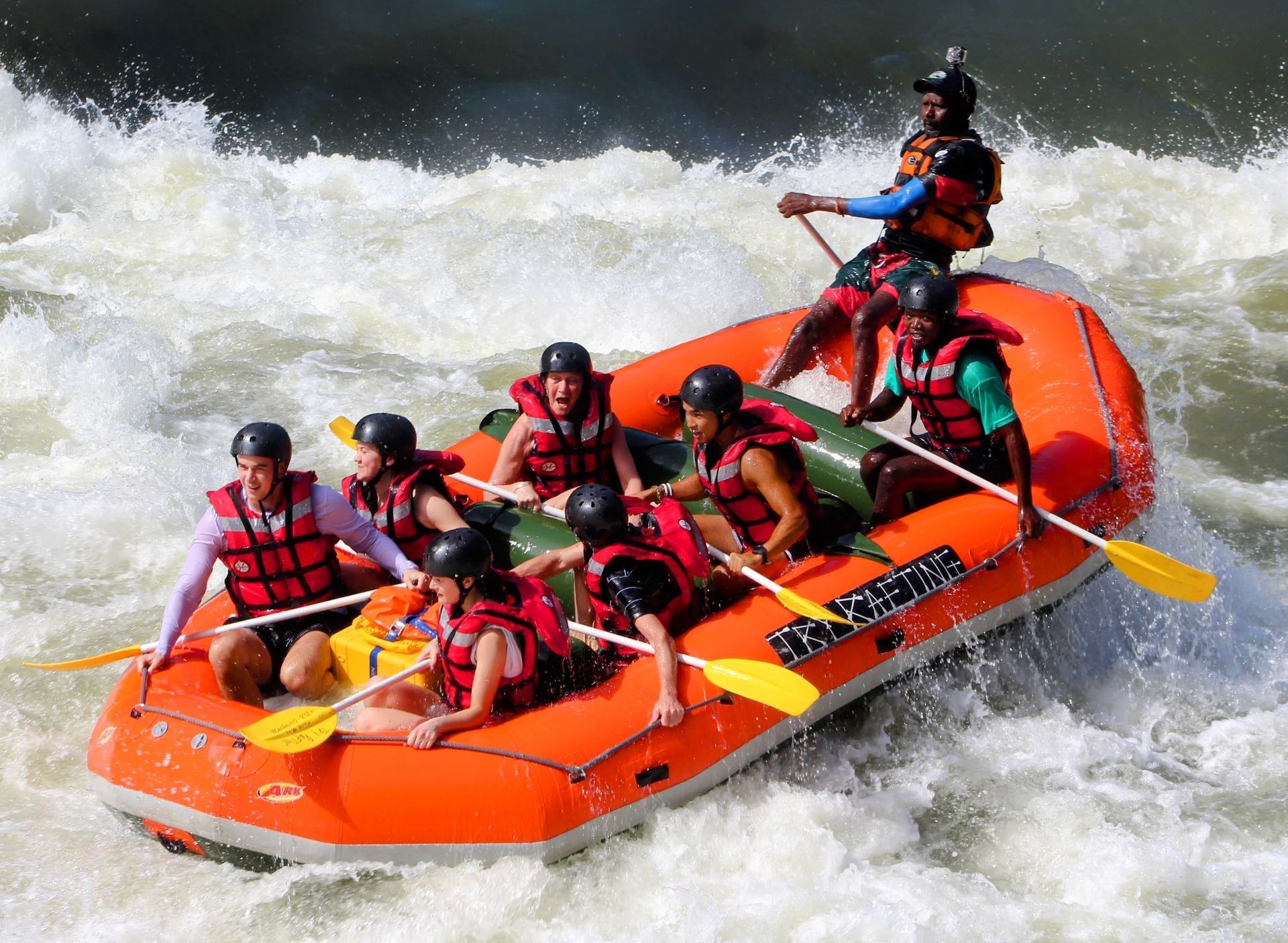 A group of people are rafting down a river in an orange raft.