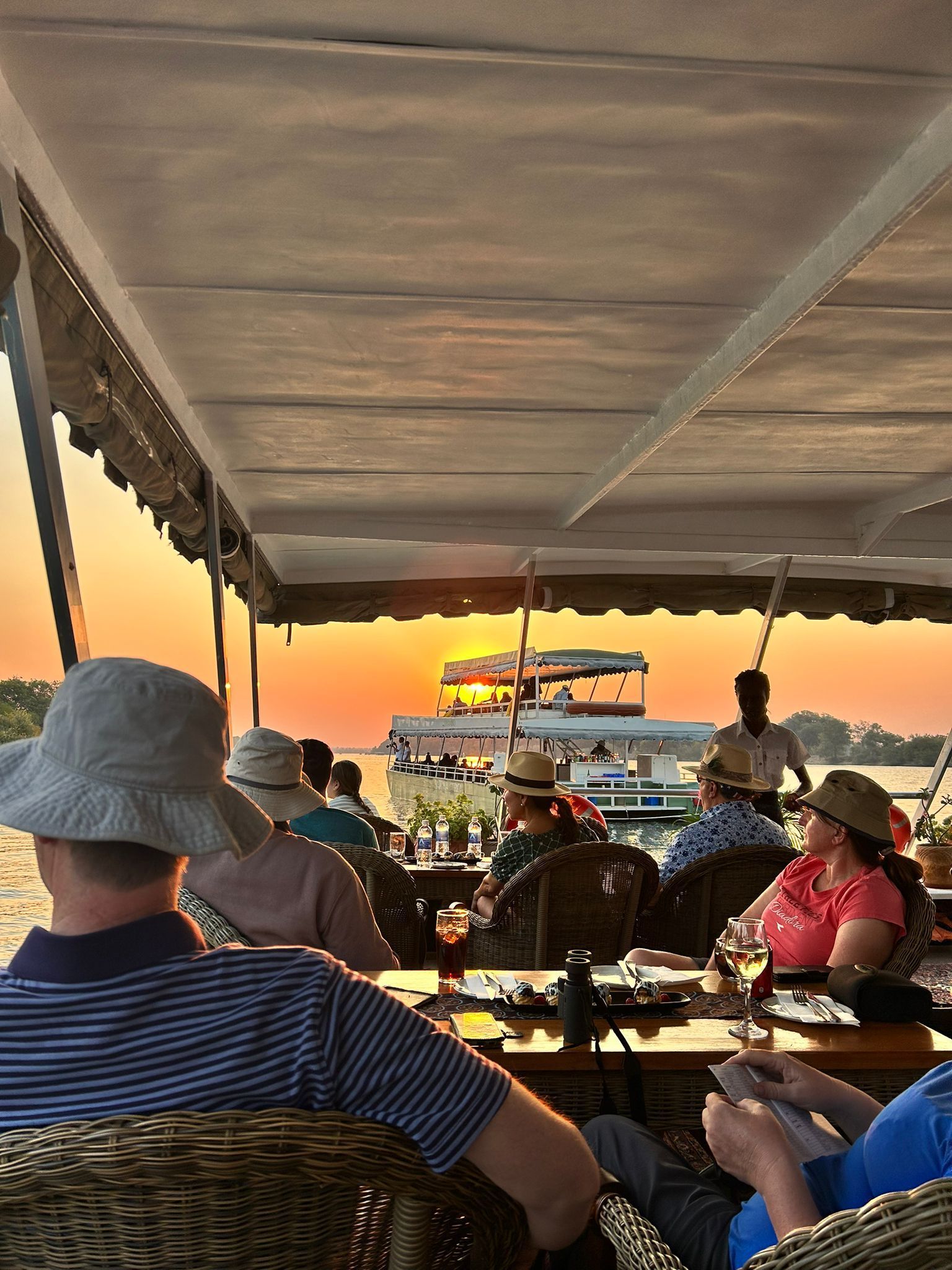 A group of people are sitting at tables on a boat at sunset.