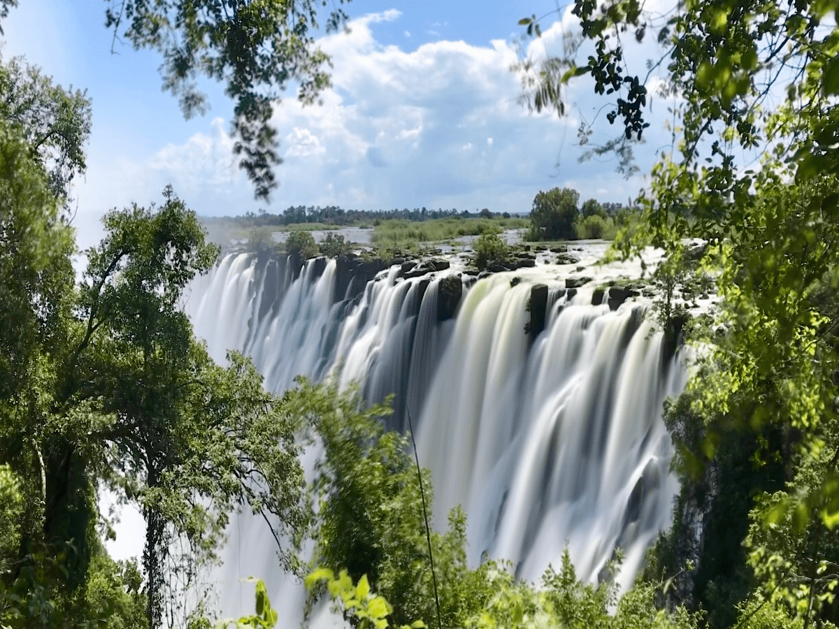 A waterfall is surrounded by trees on a sunny day.