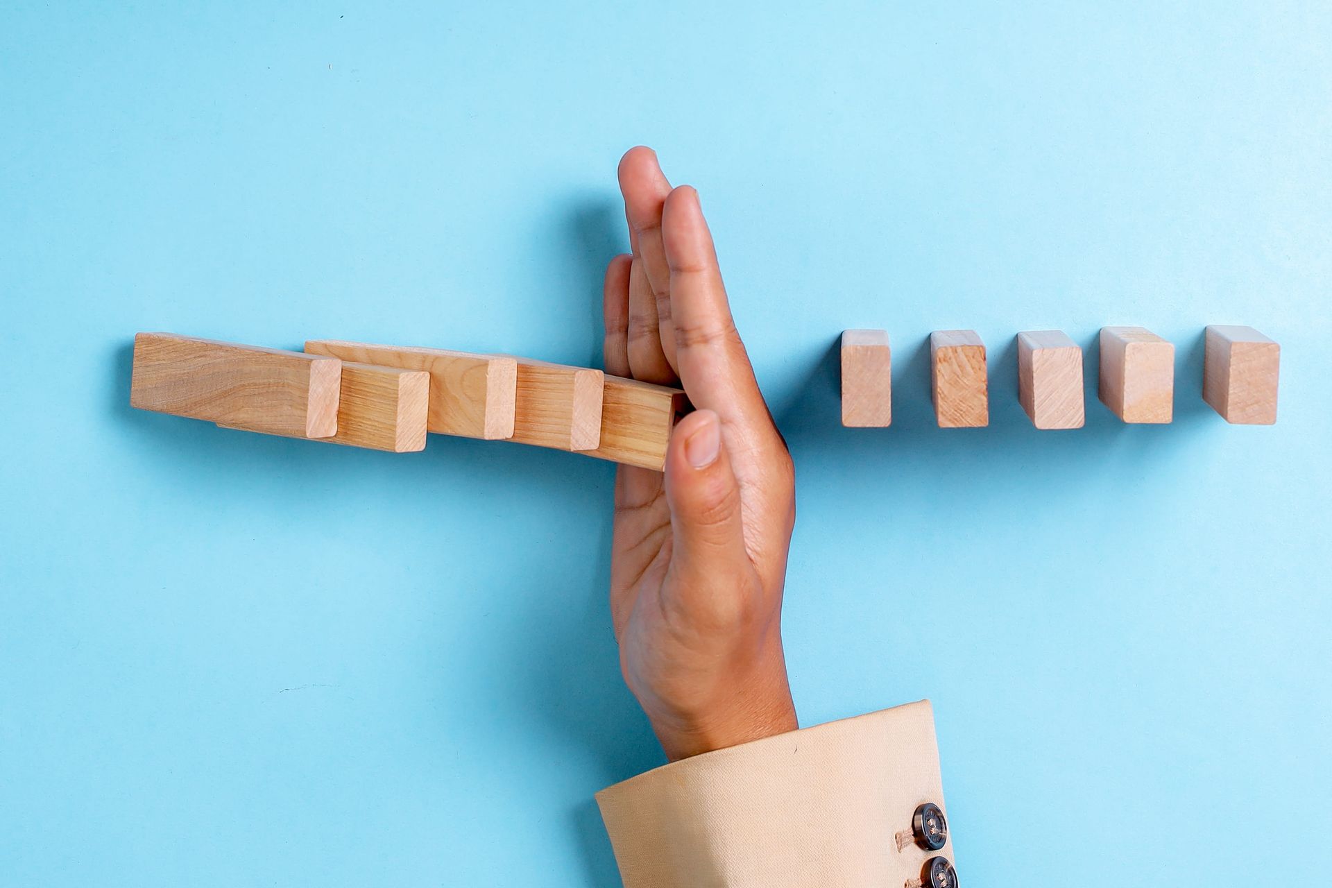 Hand stopping a wooden domino line on a blue background
