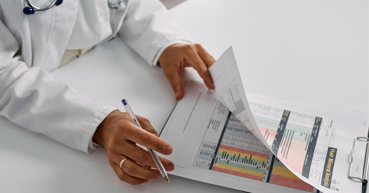 Doctor in white coat reviewing charts and writing notes at a desk.