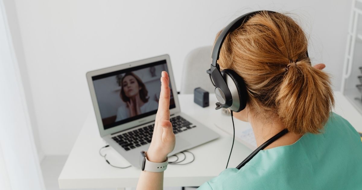 Person wearing headphones waves during a video call on a laptop in a bright room.