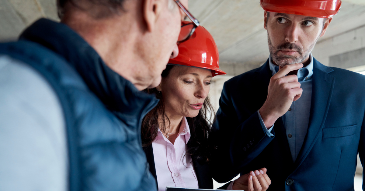 Three people in hard hats reviewing plans at a construction site