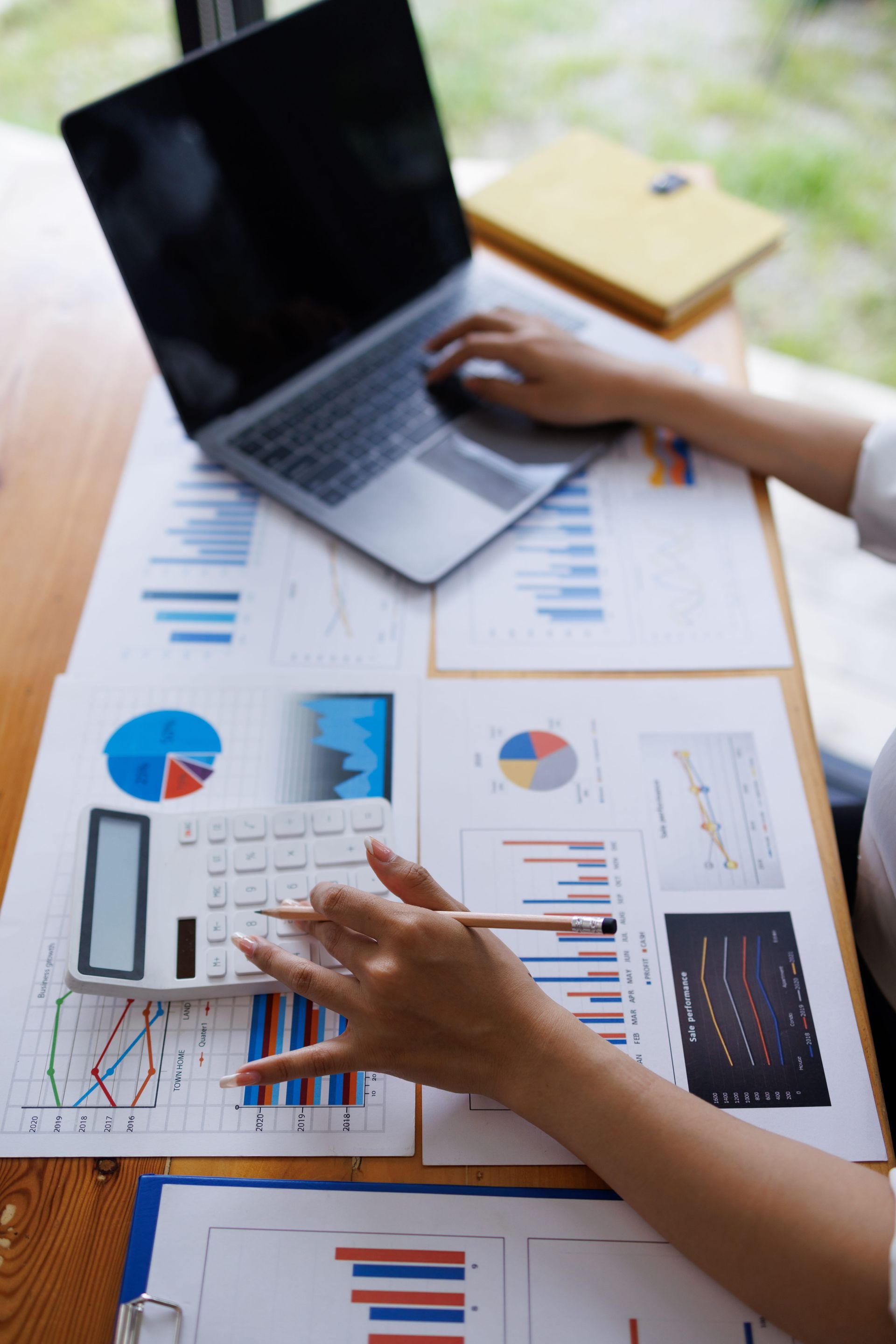 Hands analyzing charts and graphs beside a laptop on a desk