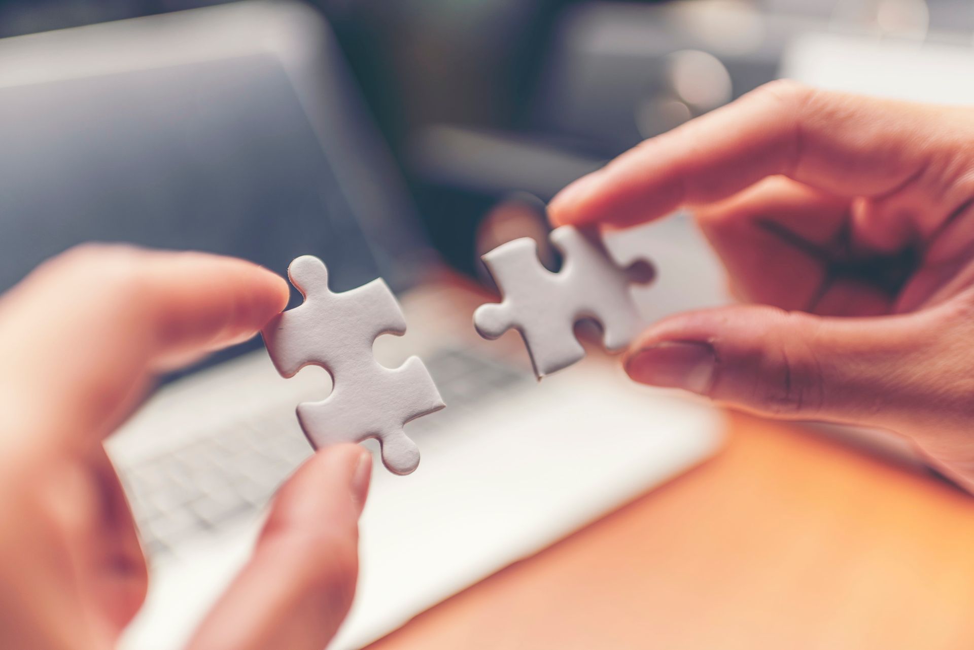 Hands holding two white puzzle pieces apart over a blurred laptop keyboard