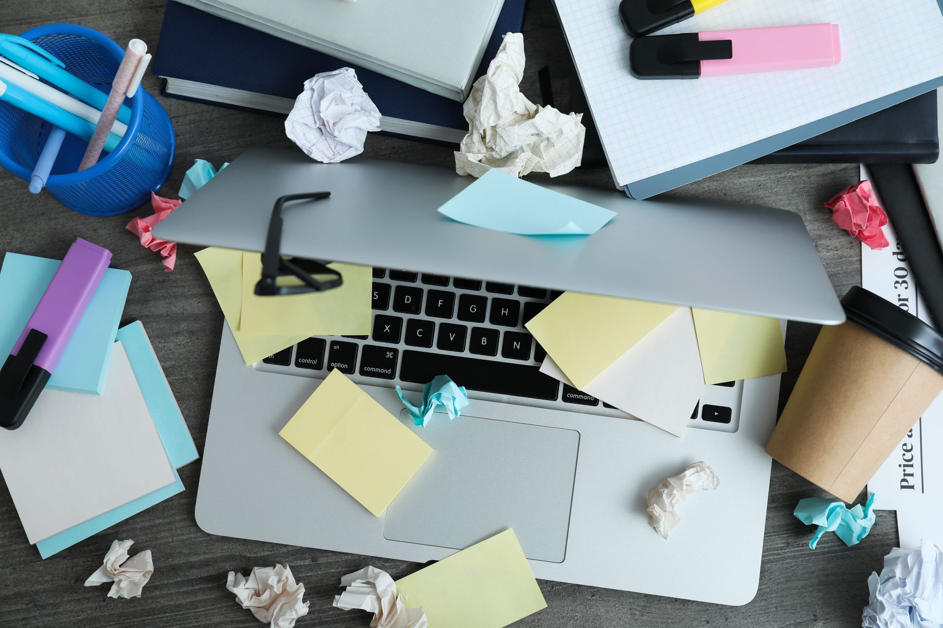 Laptop covered with sticky notes and office clutter on a desk