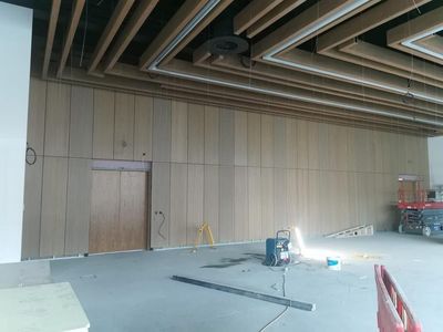 Empty interior under construction with wood-paneled wall, exposed ceiling beams, and work lights on the floor
