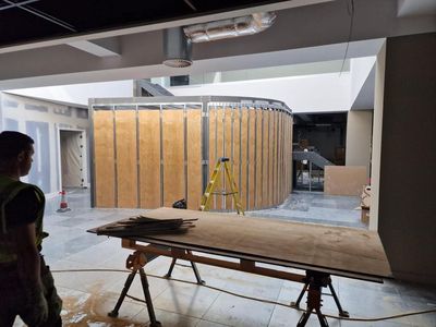 Construction site with wood-paneled curved wall, scaffolding, and a workbench in the foreground