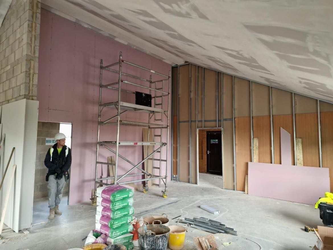 Interior under renovation with scaffolding, exposed wall framing, and a worker near an open doorway.