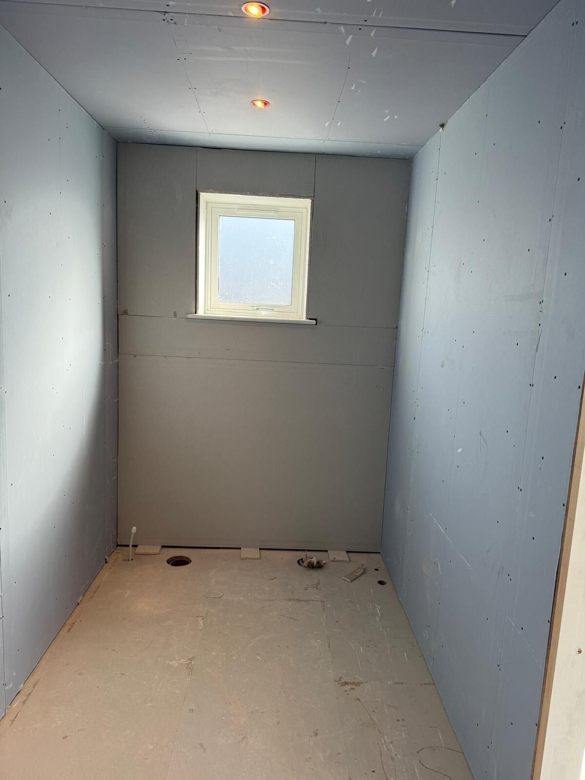 Empty narrow room with gray walls, white floor, and a small window at the far end.