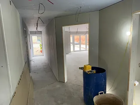 Renovation site with unfinished drywall, exposed wiring, and a blue trash bin in a narrow hallway