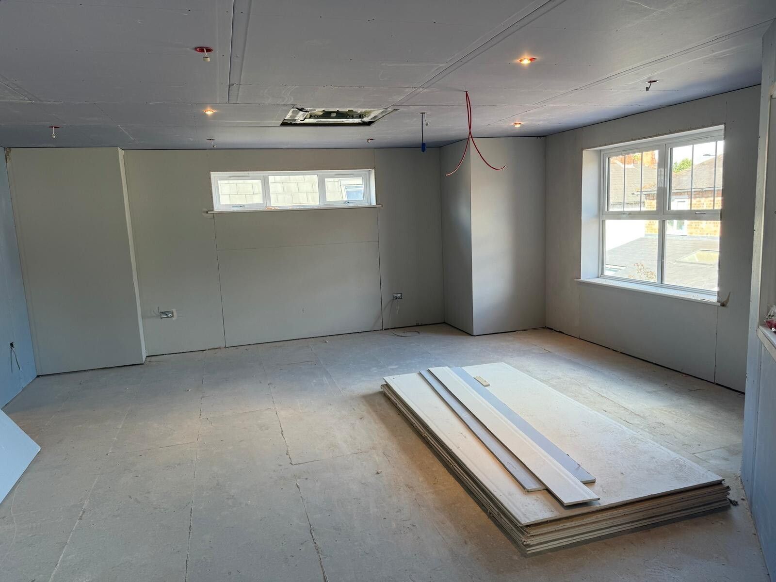 Empty unfinished room with gray walls, white ceiling, windows, and stacked drywall on the floor