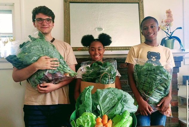 Three people are standing next to each other holding bags of vegetables.