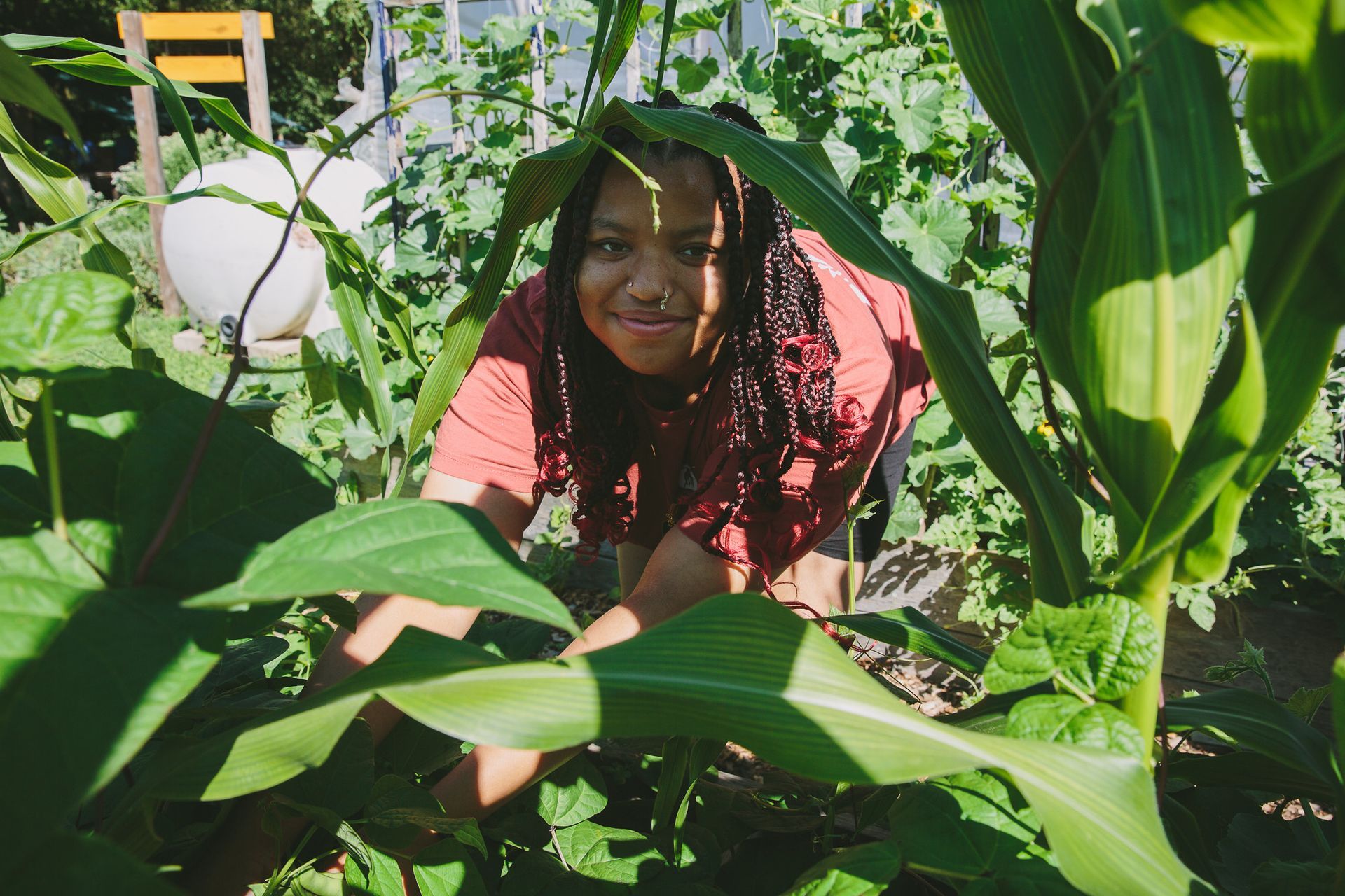 A woman is kneeling down in a garden surrounded by plants.