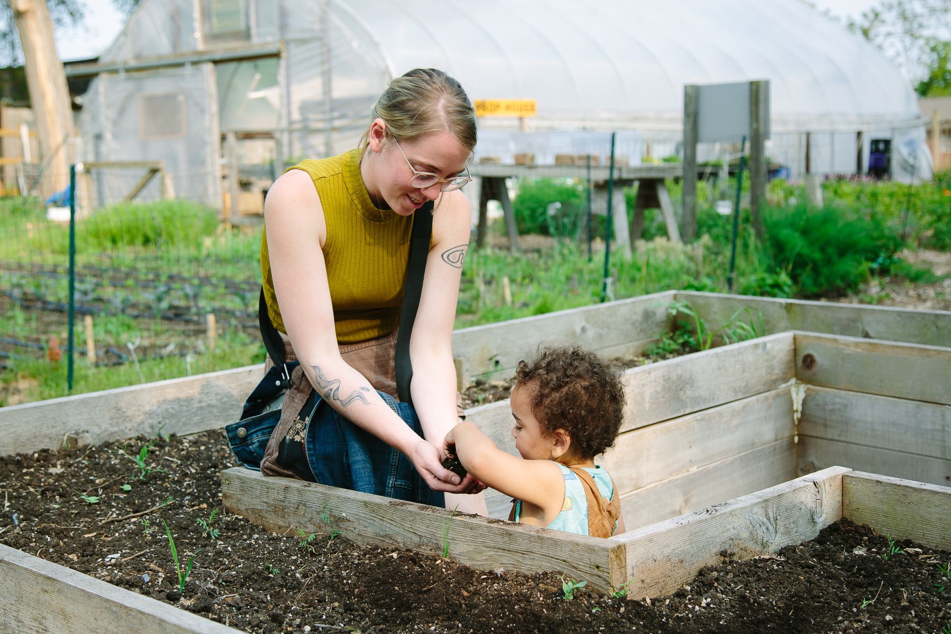 A woman and a child are sitting in a wooden box in a garden.