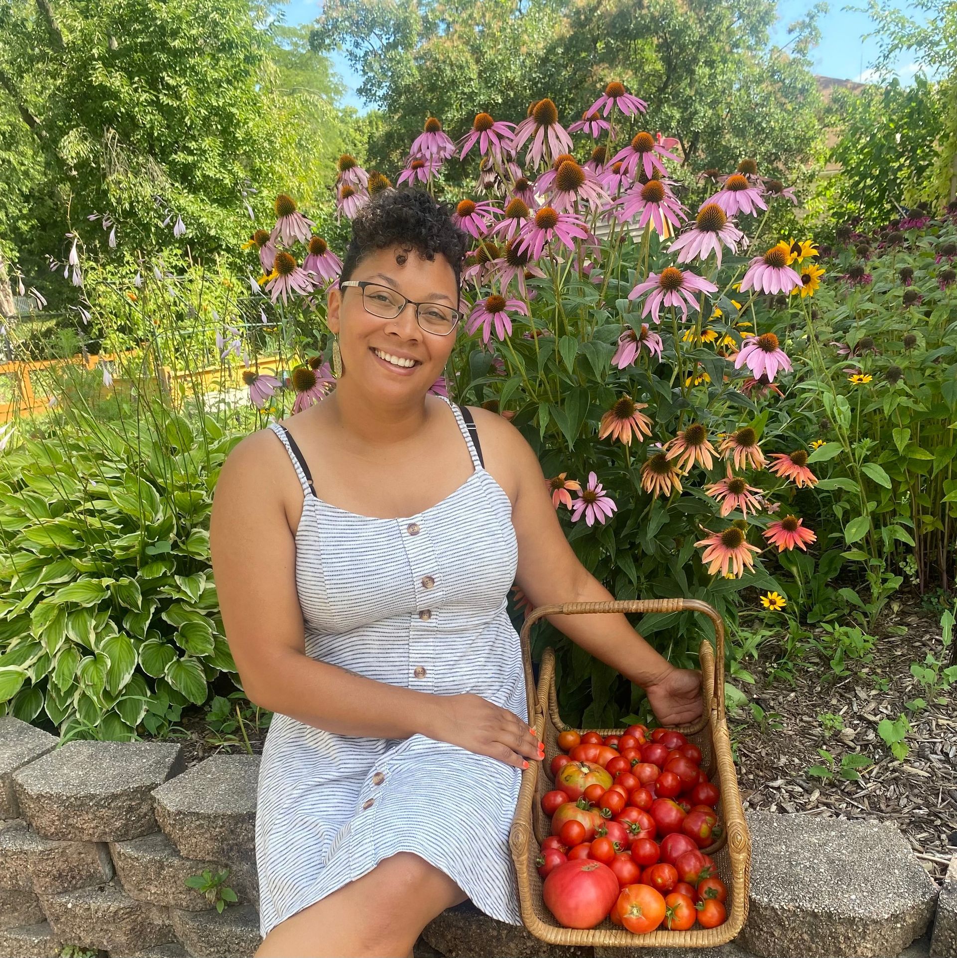 A woman is sitting on a stone wall holding a basket of tomatoes.