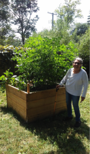 A woman is standing next to a wooden planter filled with plants.