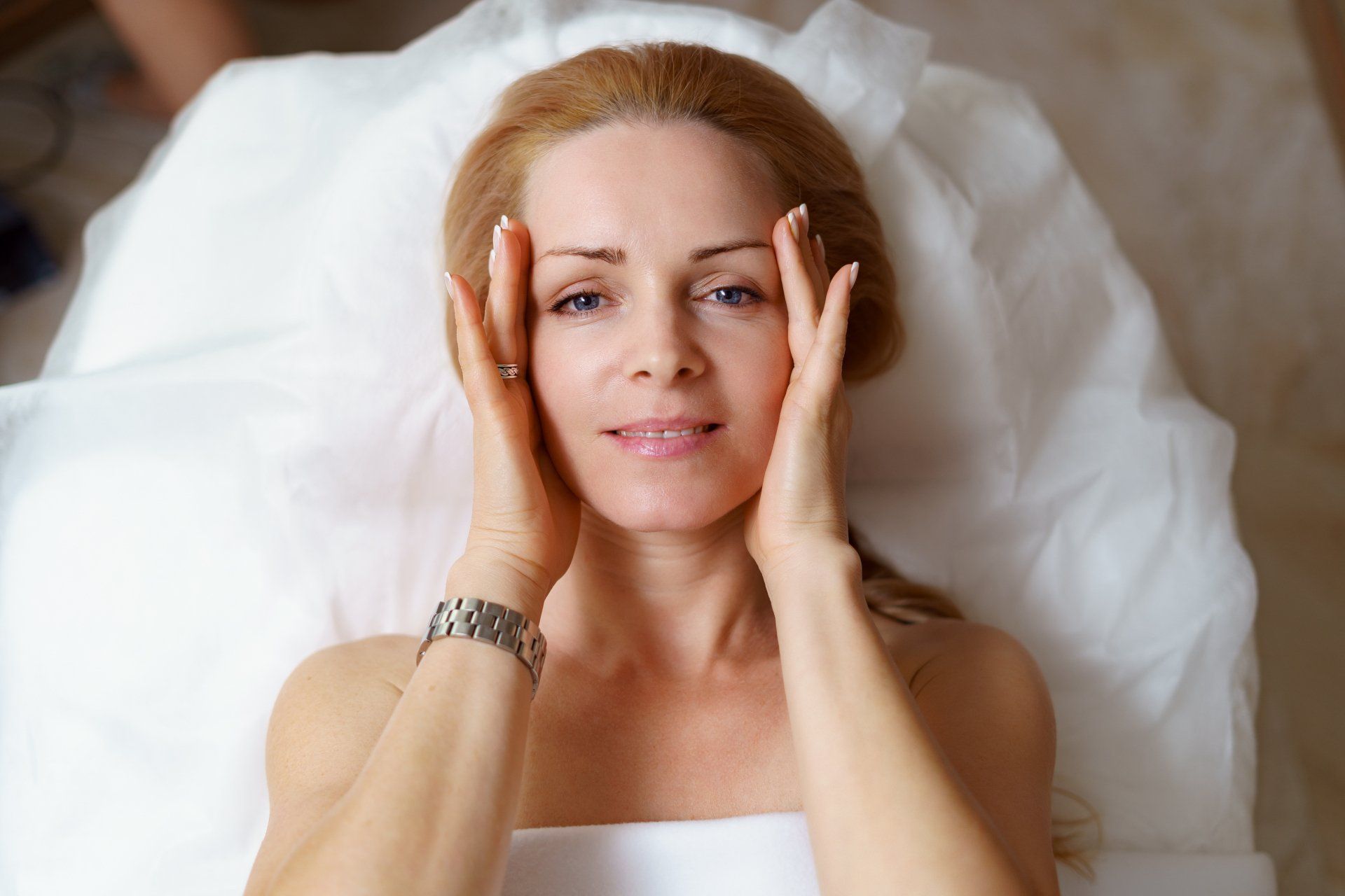 Una donna è sdraiata su un letto con le mani sul viso.