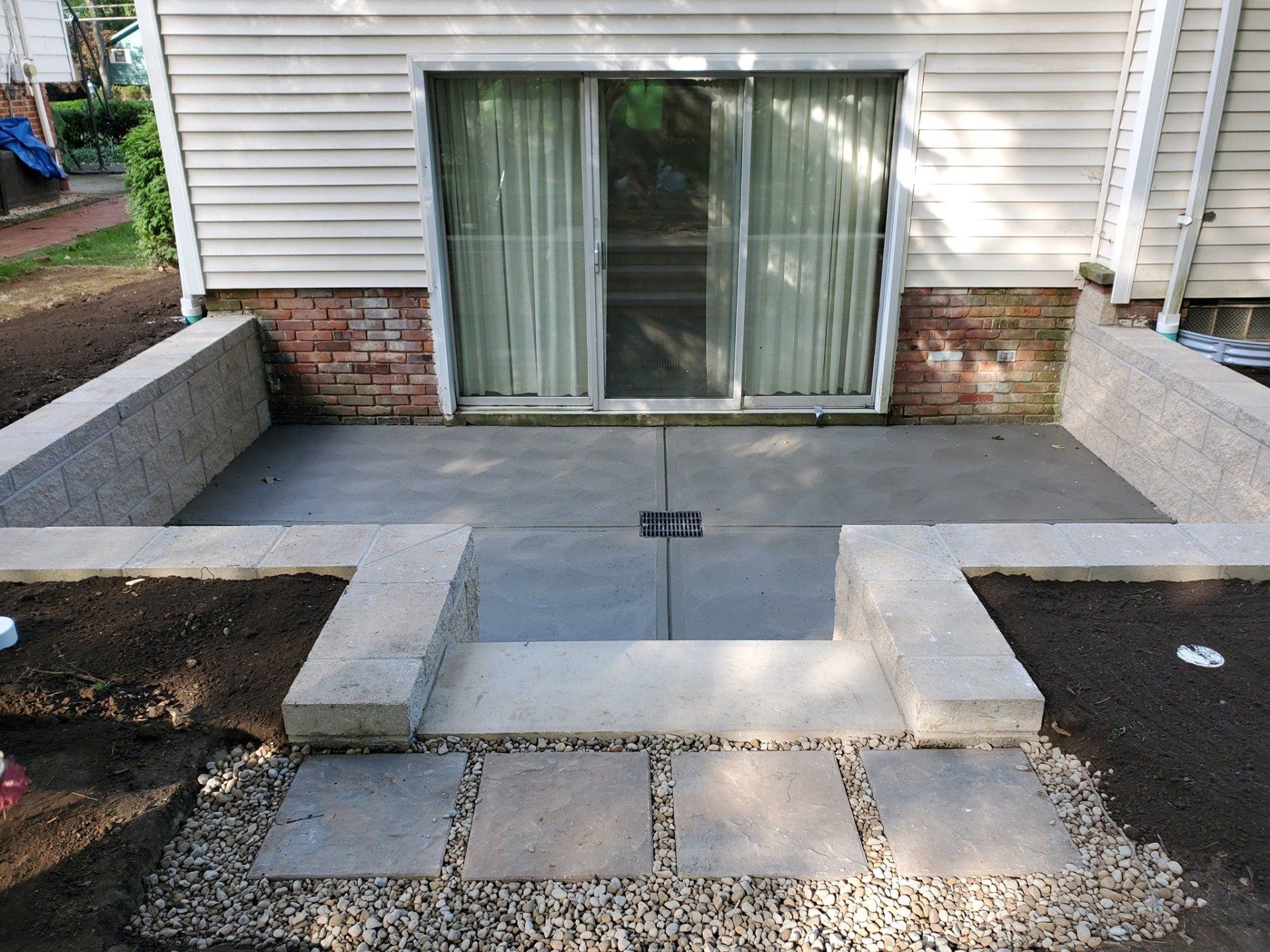 Concrete patio with sliding glass door, raised beds, steps, and gravel.