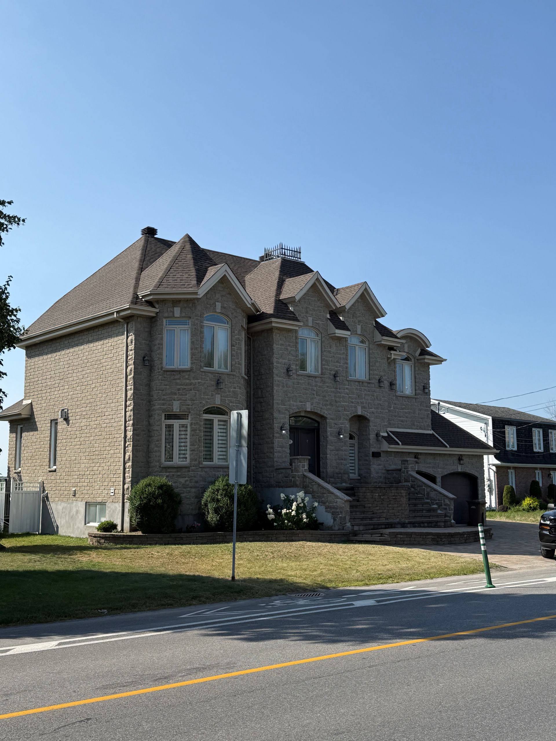 Maison en pierre à deux étages avec un toit brun par une journée ensoleillée.