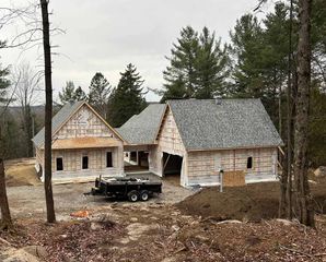 Construction d'une maison avec une caravane garée devant. Le toit est recouvert de bardeaux. Des arbres entourent le bâtiment.
