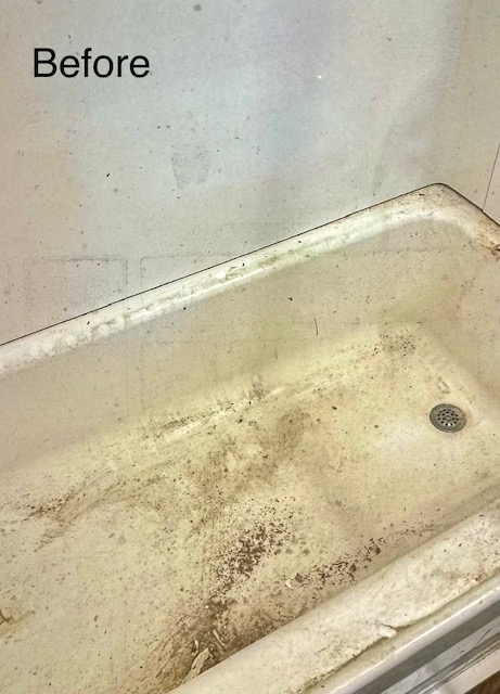 Dirty, stained, off-white bathtub with debris in the bottom and on the sides. The wall is also stained.