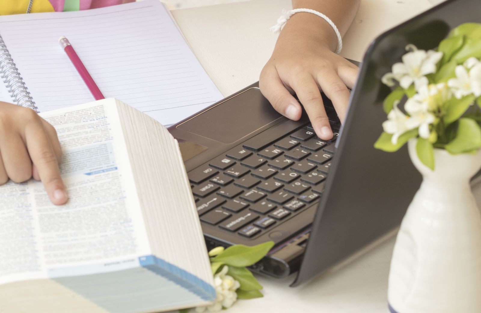mano su pc portatile mentre consulta un dizionario per le traduzioni
