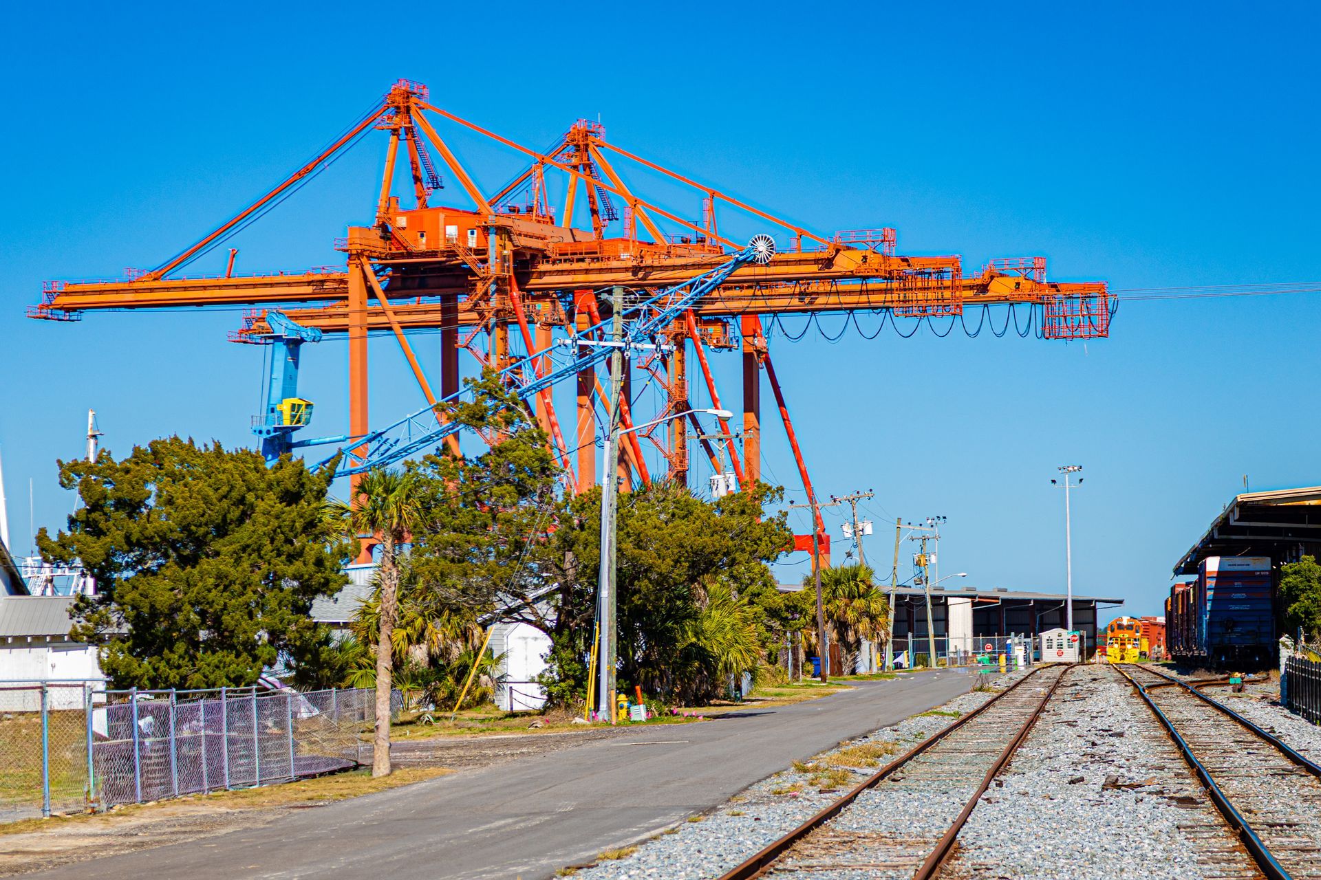 Orange cranes at a rail yard beside tracks under a clear blue sky