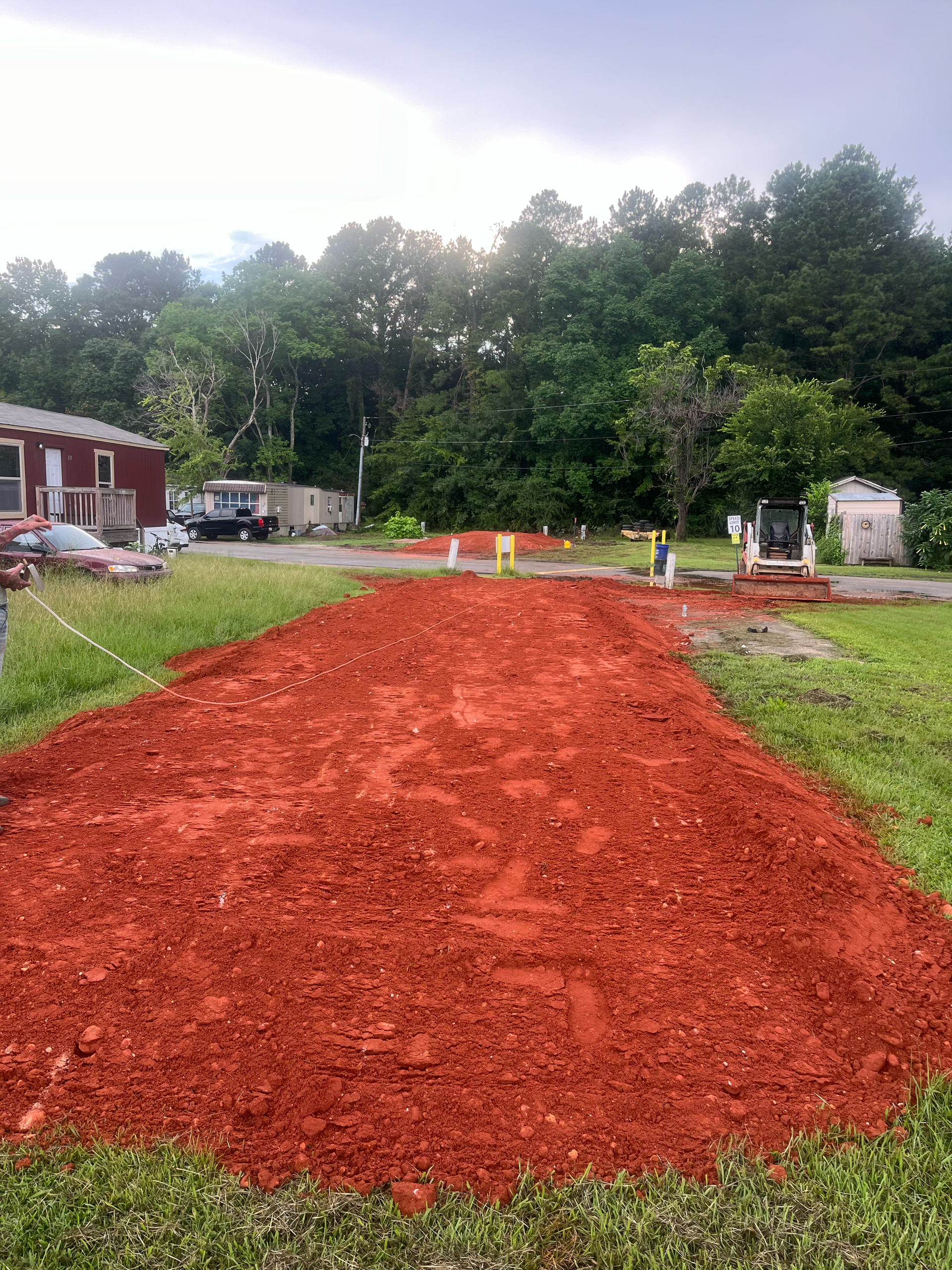 A wide patch of bright red mulch spread across a grassy yard with a small tractor and a house in the background.