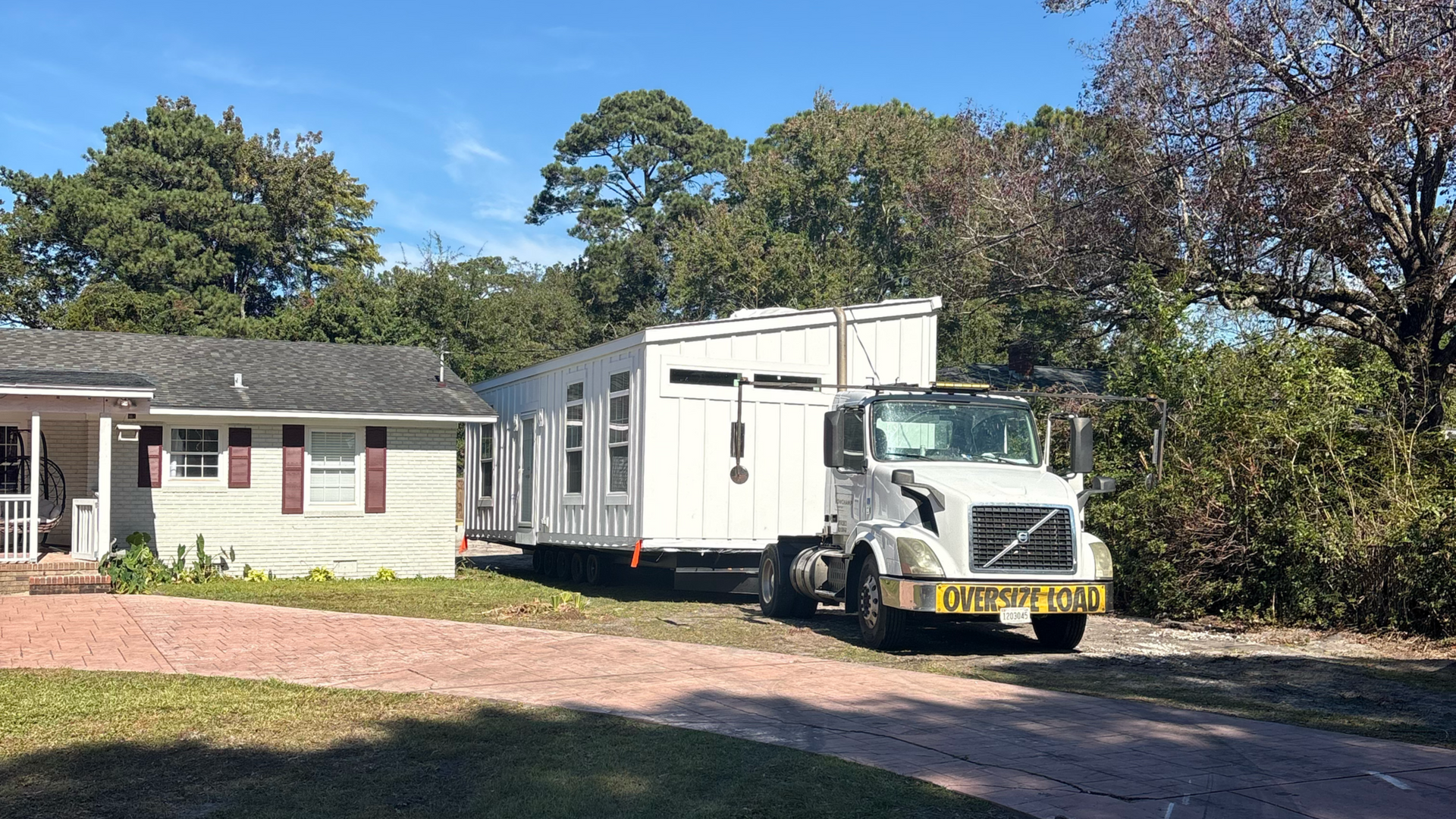 White box truck parked beside a small house on a sunny day with trees in the background